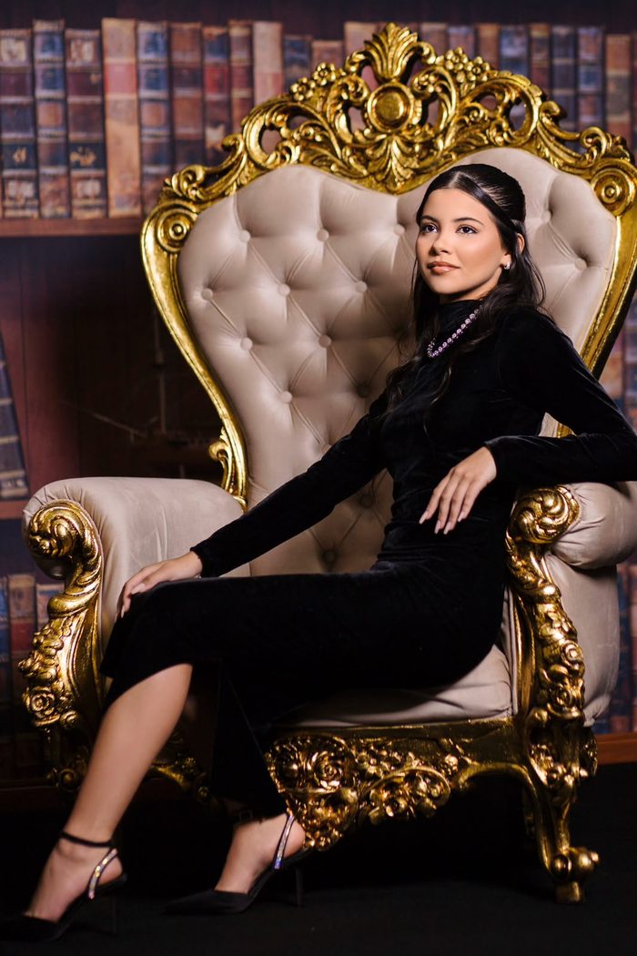 Formanda posando em poltrona dourada em cenário de biblioteca